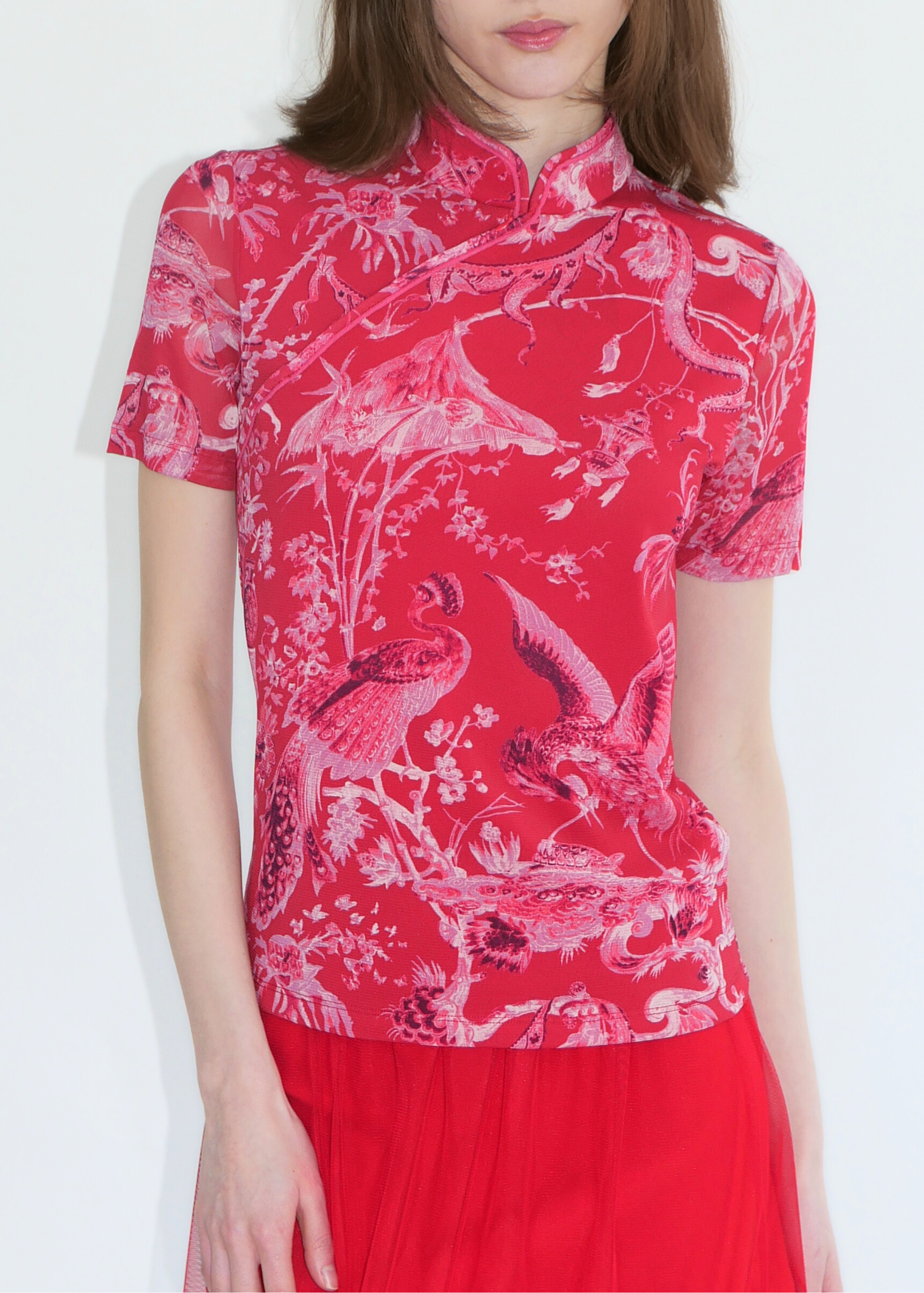 Woman wearing a red floral and bird blouse with a white background