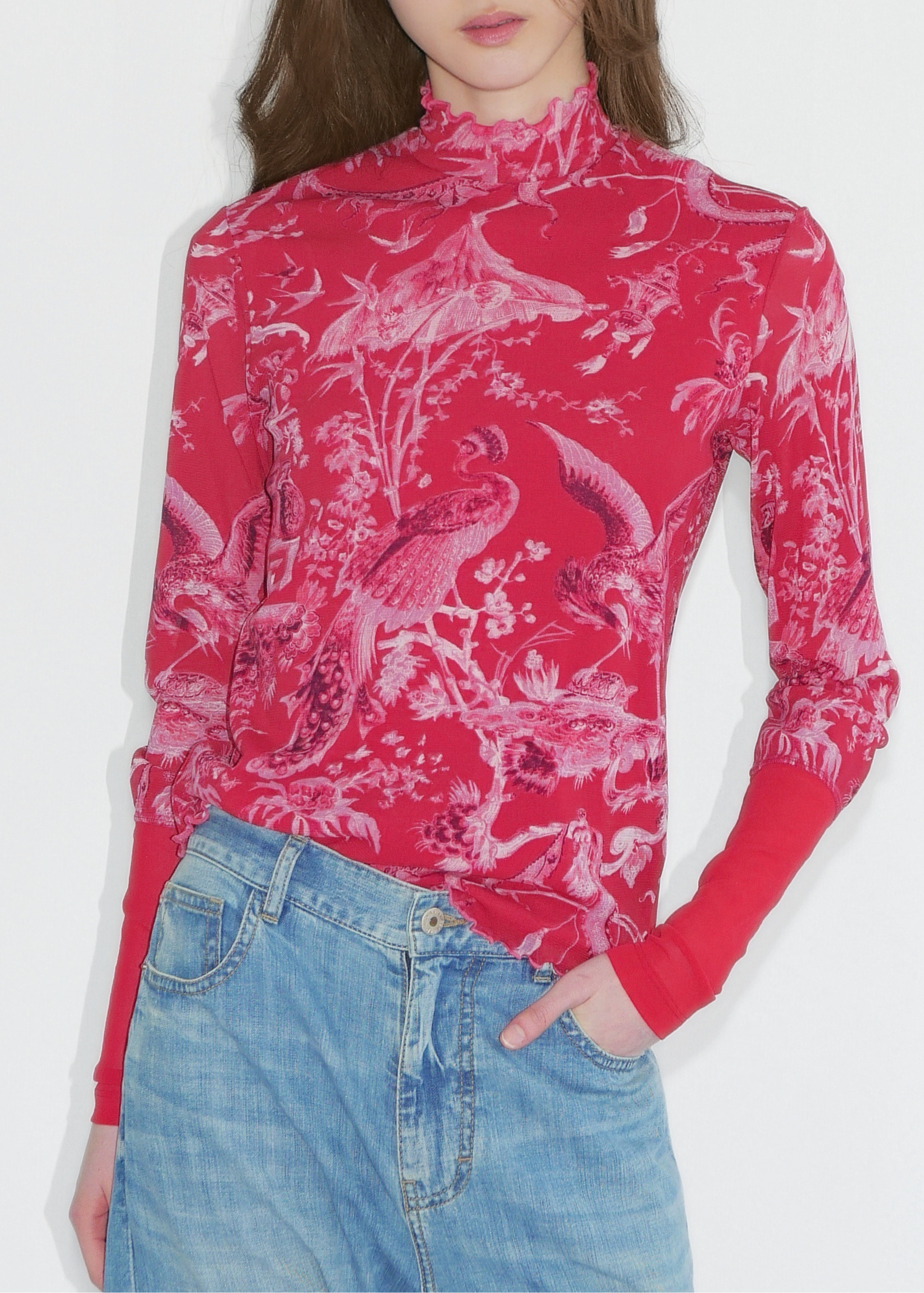 Person wearing a red patterned long-sleeve top and blue jeans on a white background