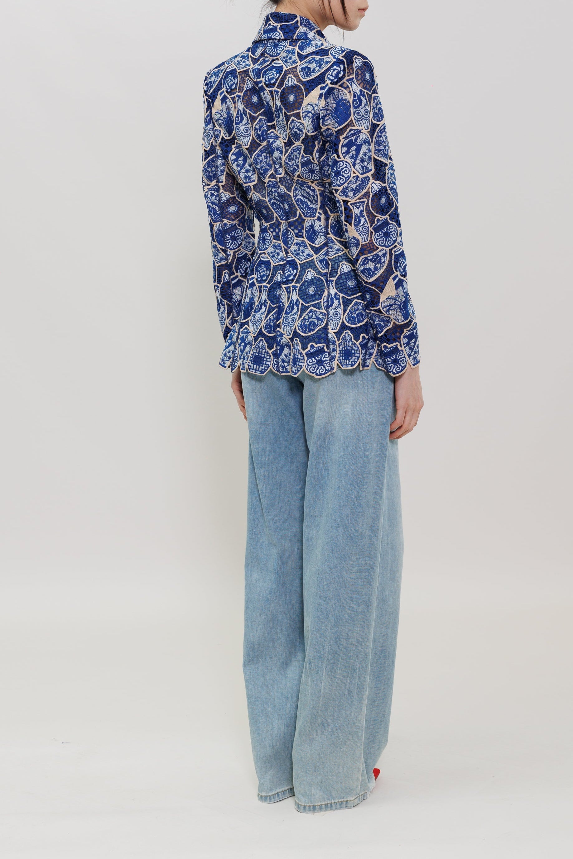A model is shown from the back wearing a blue and white patterned long-sleeve shirt and light blue wide-leg jeans against a plain white studio background.