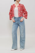 A woman modeling a red and white floral patterned cropped jacket over a white top, paired with light blue wide-leg jeans and white pointed shoes, against a plain light gray studio background.