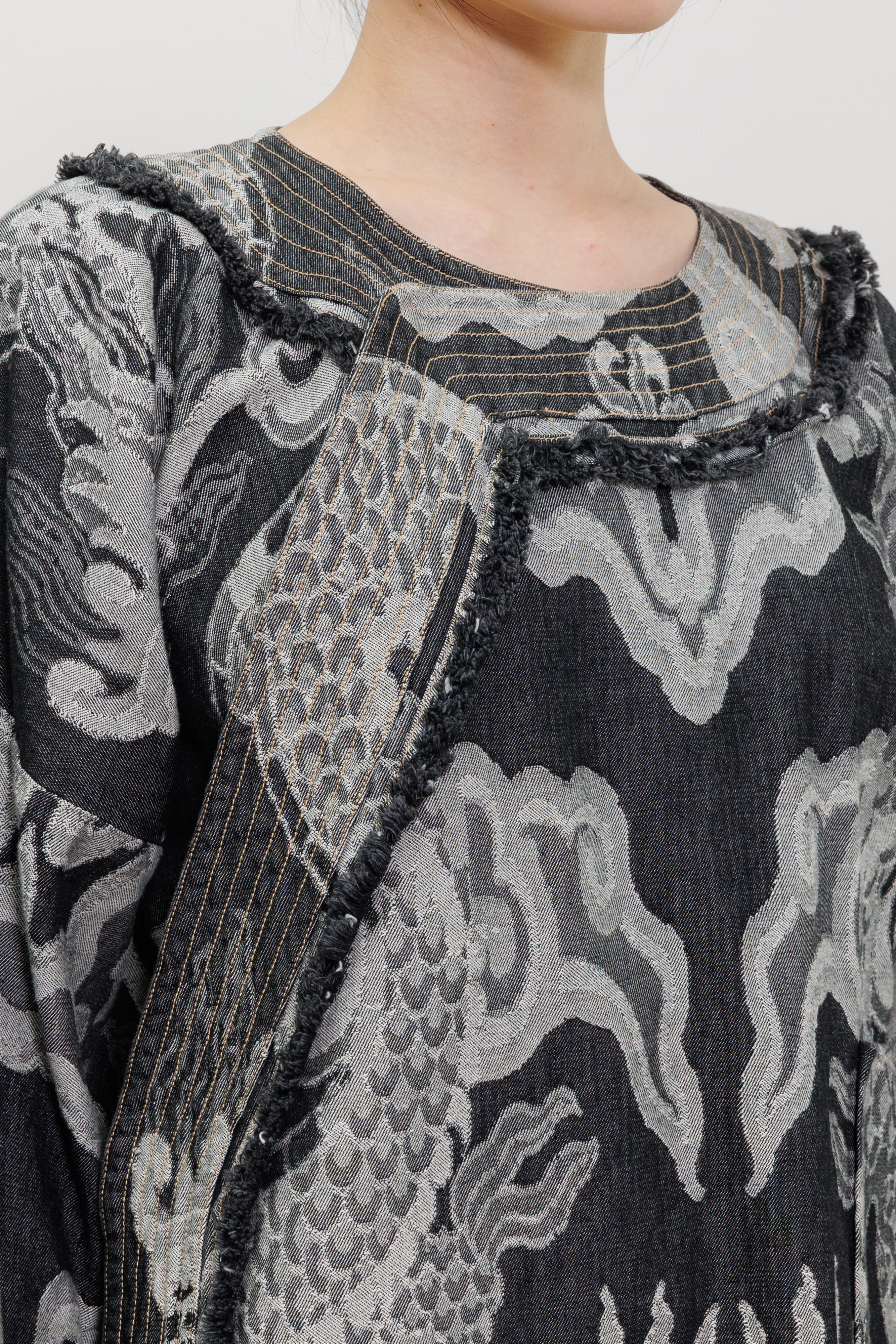 Close-up of a person wearing a dark gray and light gray patterned top with frayed trim and a round neckline.
