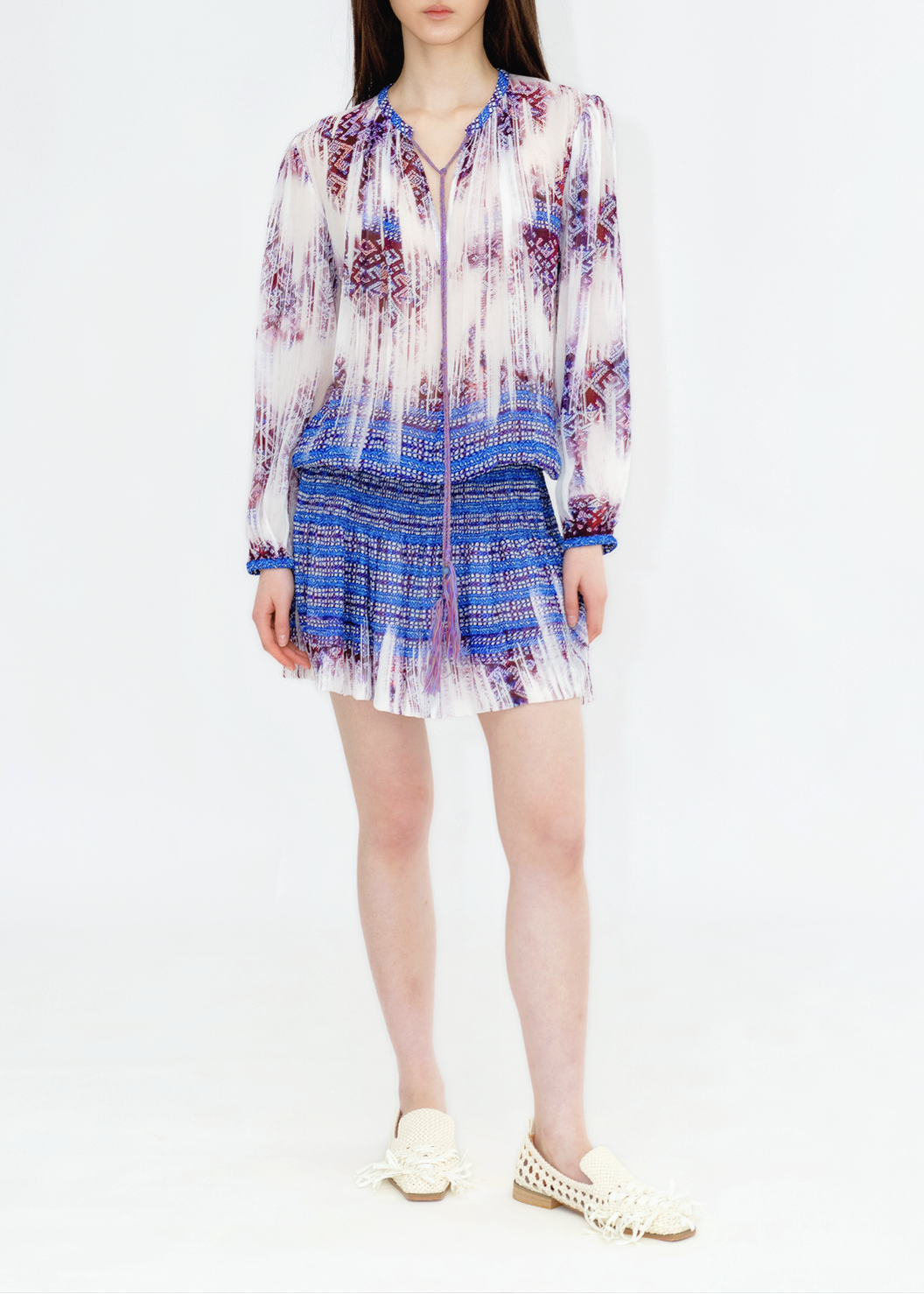 A woman standing against a white background wearing a multicolored floral print dress with long sleeves and a V-neck neckline.