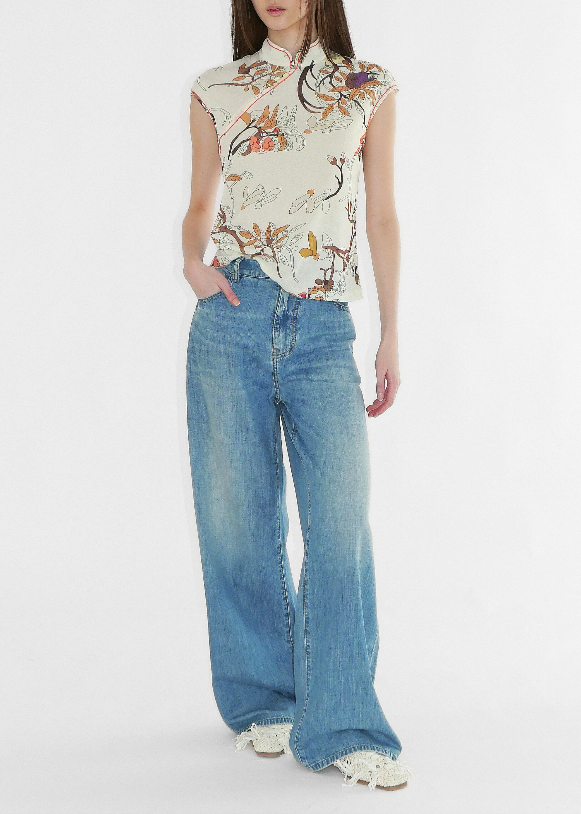 Woman wearing a floral sleeveless top and blue jeans on a white background