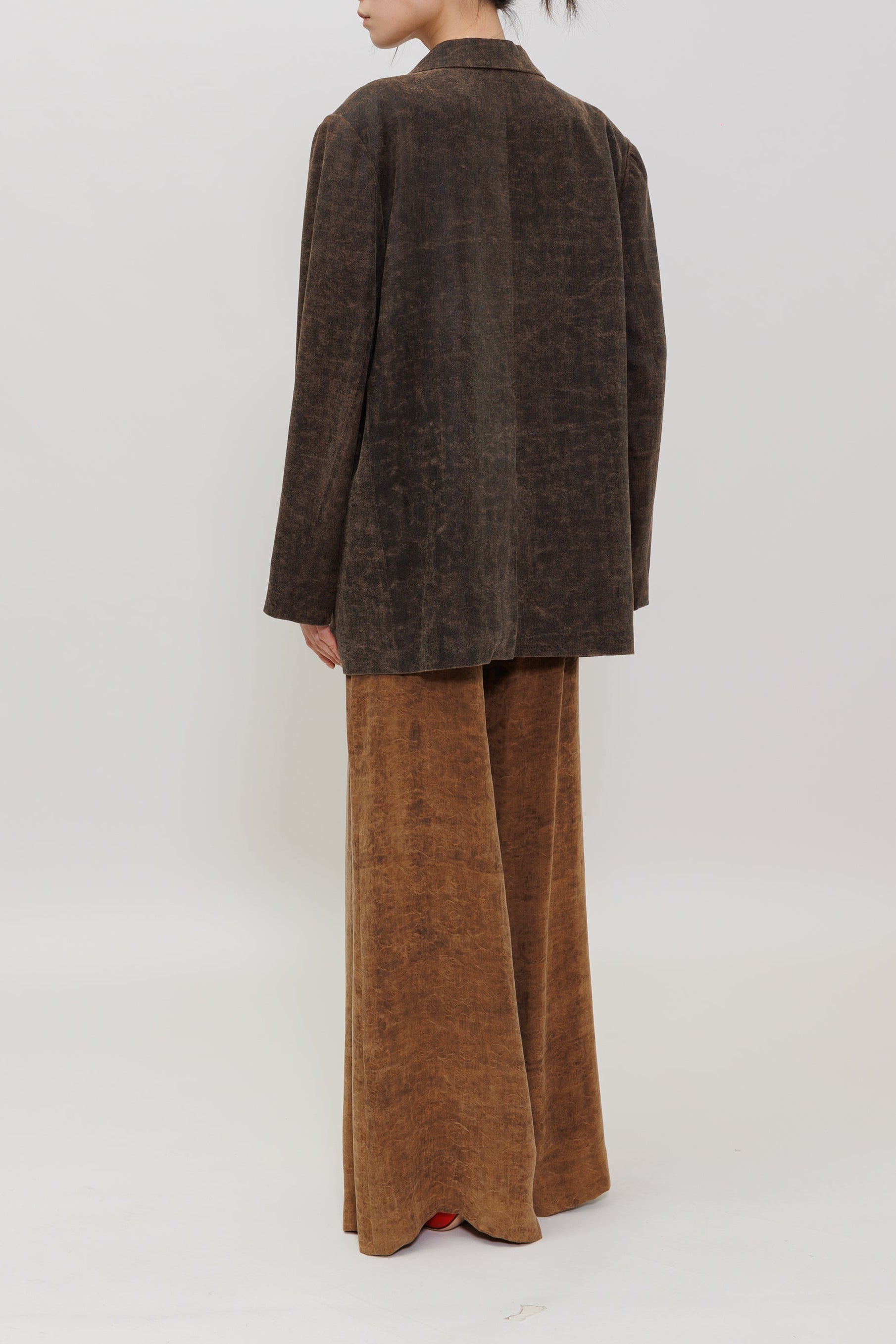 A model is shown from the back wearing a dark brown textured blazer and matching wide-leg trousers against a plain light gray studio background.