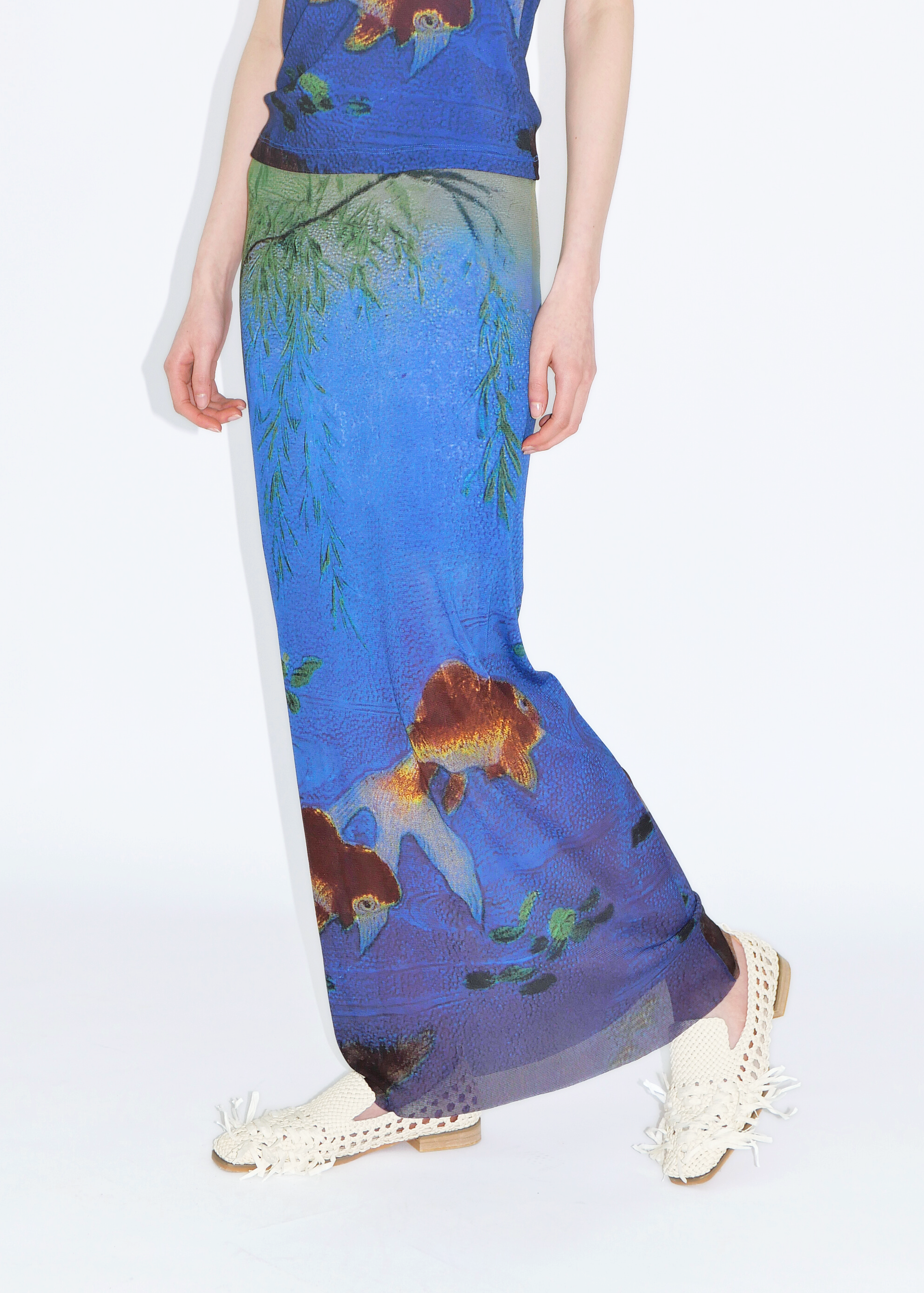 A person wearing a long skirt with a blue netting design and goldfish prints.