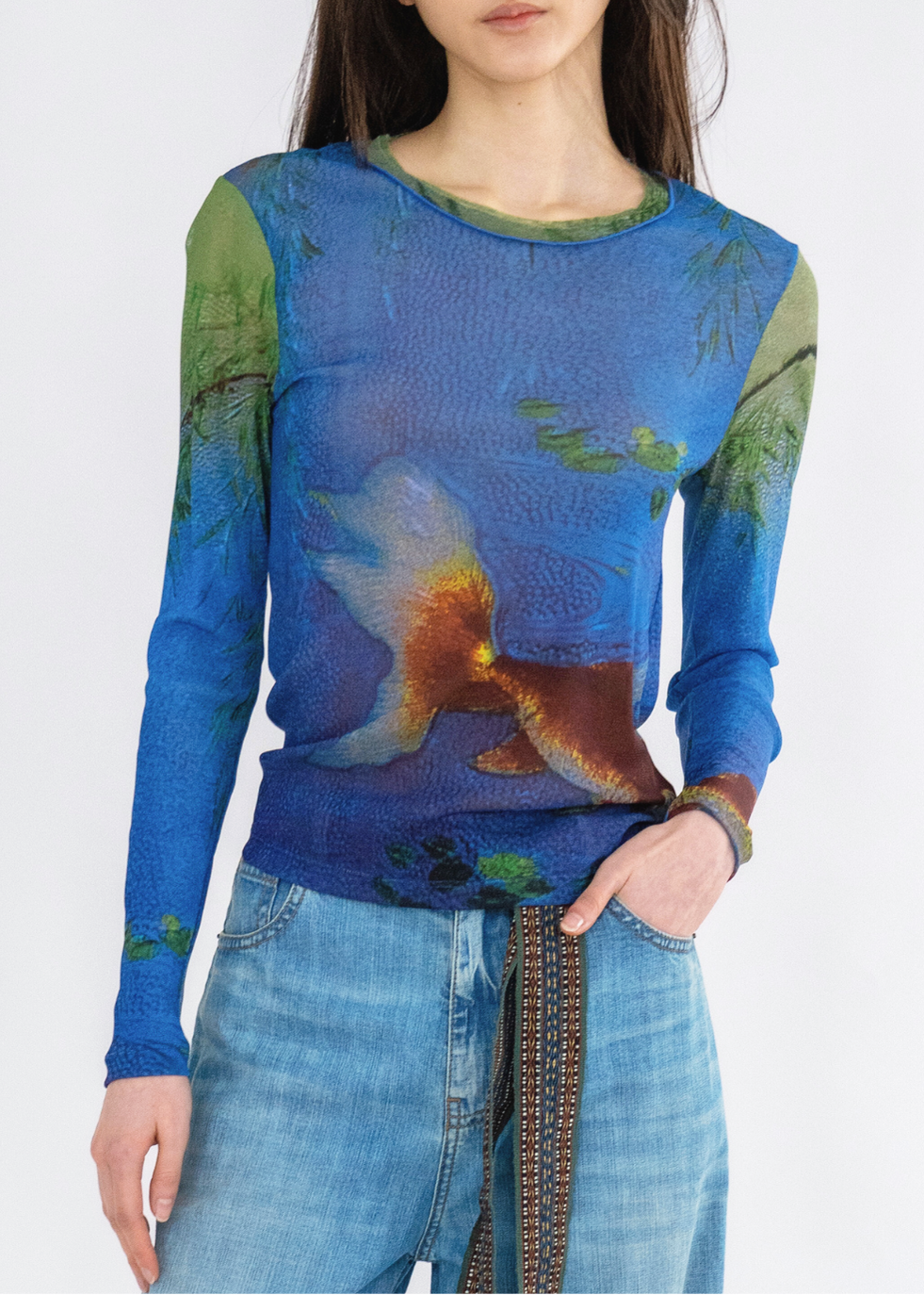 A woman wearing a long-sleeved, blue and green, floral and goldfish printed top with round neckline, paired with blue jeans.