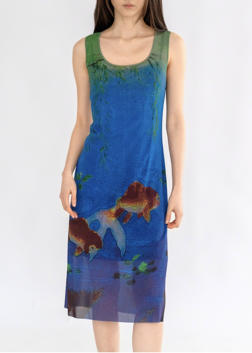 A woman standing against a white background wearing a sleeveless knee-length dress with a multicolored floral pattern.