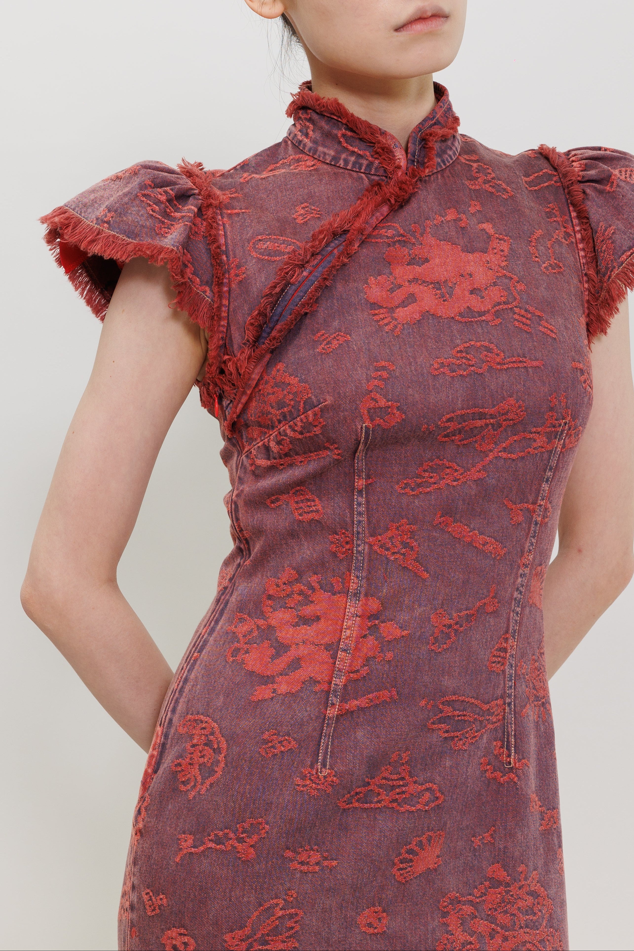 A close-up of a model wearing a dark red and purple denim cheongsam dress with red embroidered dragon patterns and frayed collar details.