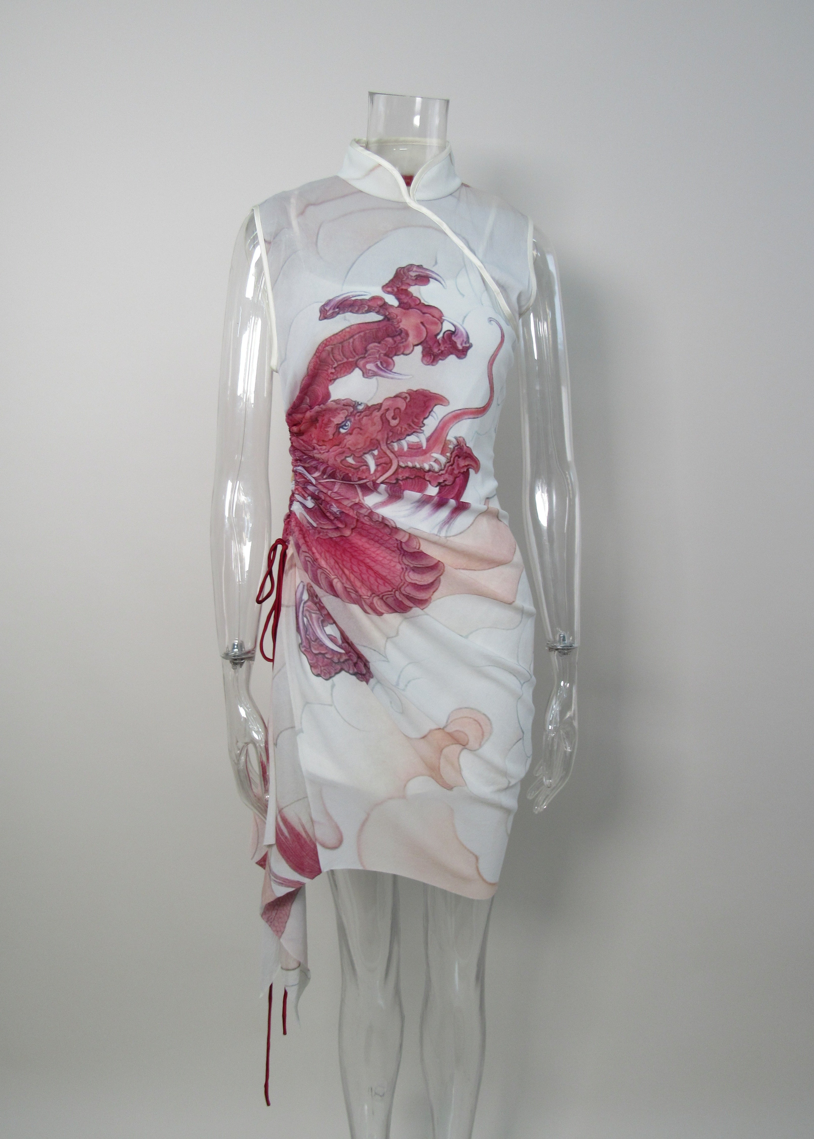 A sleeveless white dress displayed on a clear mannequin, featuring a large red and pink abstract fish-like print on the front and a white collar with a tie closure.