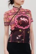 A model wearing a short-sleeved black midi skirt paired with a pink and black patterned top, styled with black pointed-toe heels against a light gray studio background.