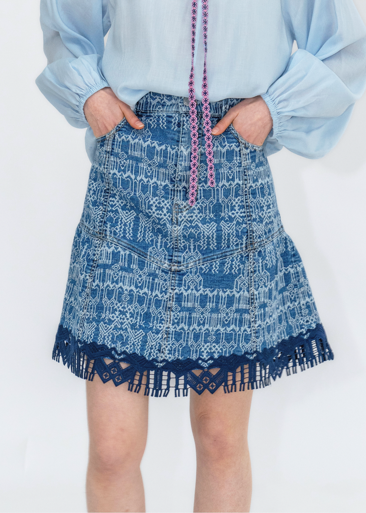 A person wearing a blue denim mini skirt with a geometric pattern and lace detailing at the hem.