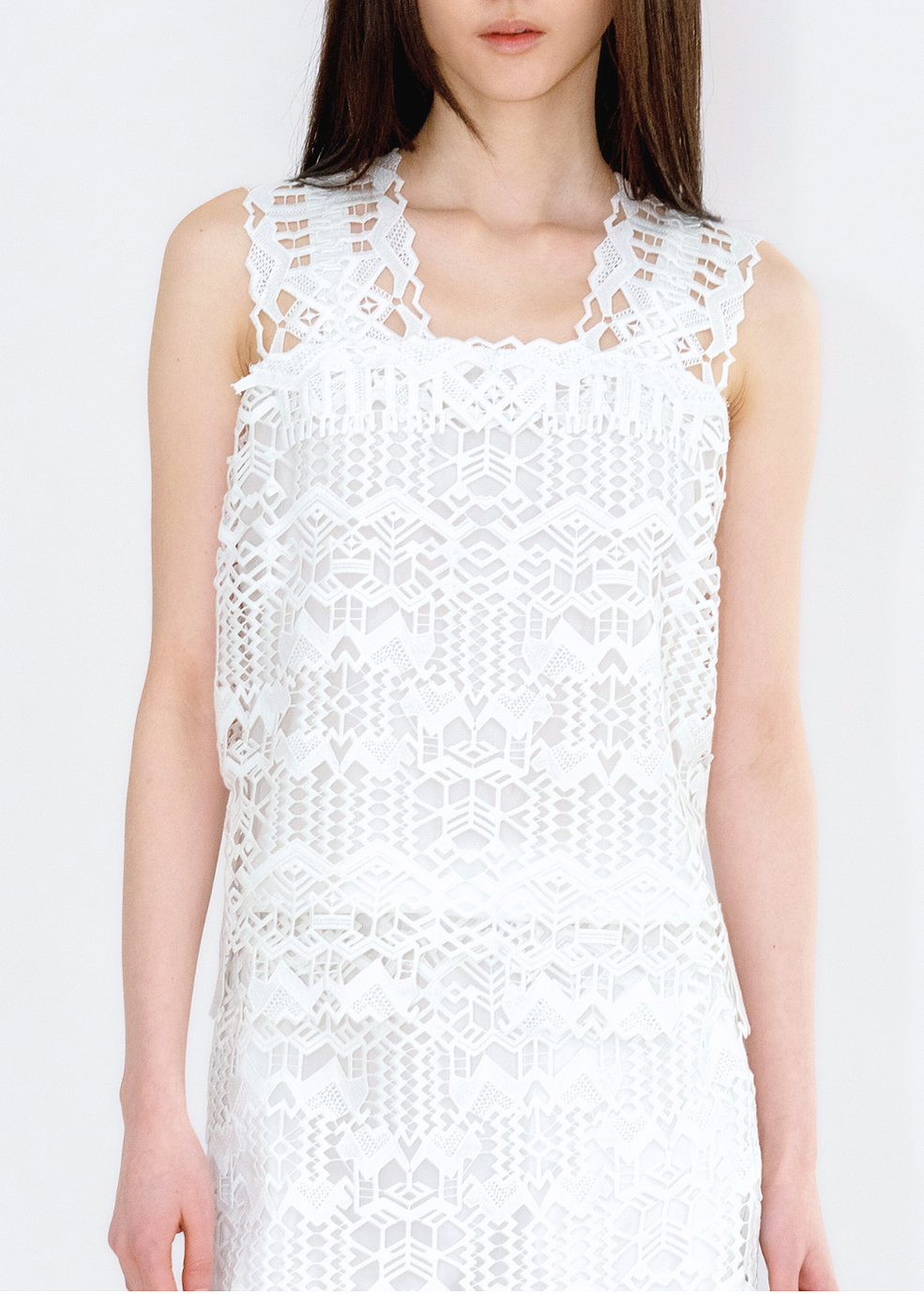 A woman wearing a white sleeveless tank top with deer and brocade inspired lace patterns.