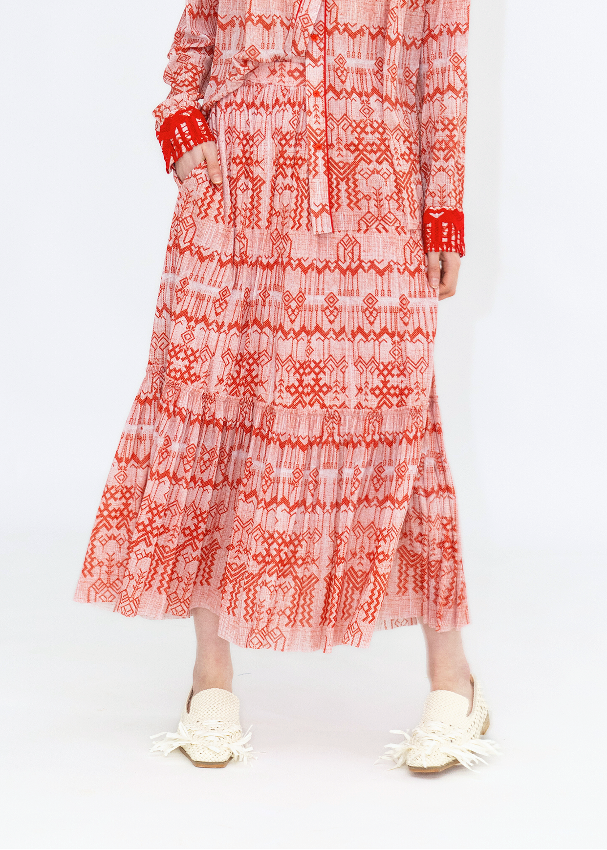 A person wearing a long skirt with a red and white deer print, paired with a red top and white shoes.