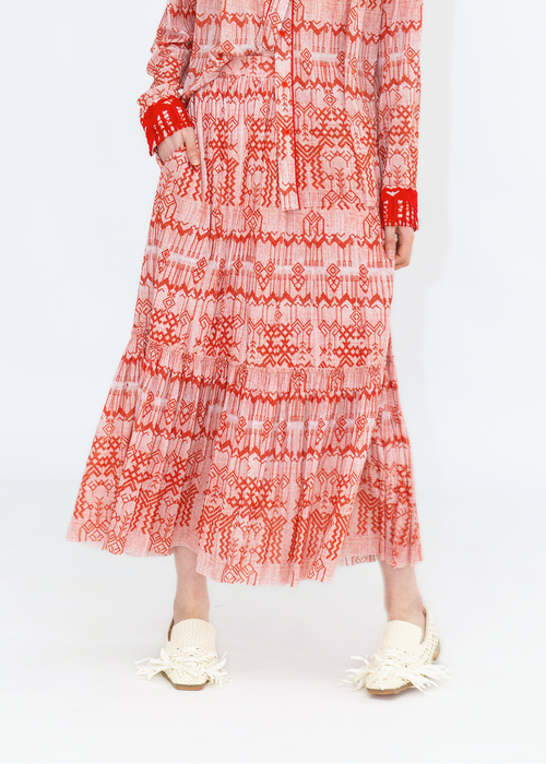A person wearing a long skirt with a red and white deer print, paired with a red top and white shoes.