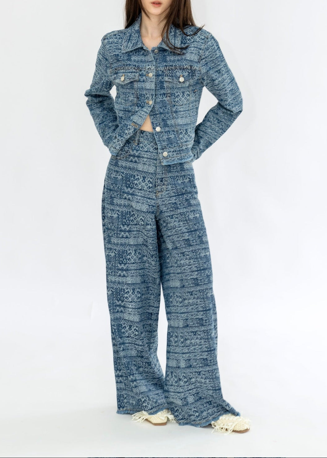 A model wearing a matching blue patterned two-piece set consisting of a cropped button-up jacket and wide-leg pants, styled with white slip-on shoes against a plain white background.