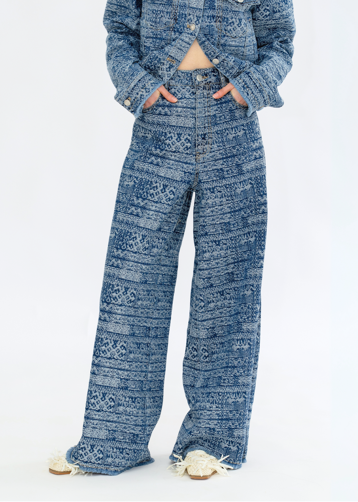 A person standing in a studio setting, wearing loose-fit blue jeans with a tie-dye stripe pattern.
