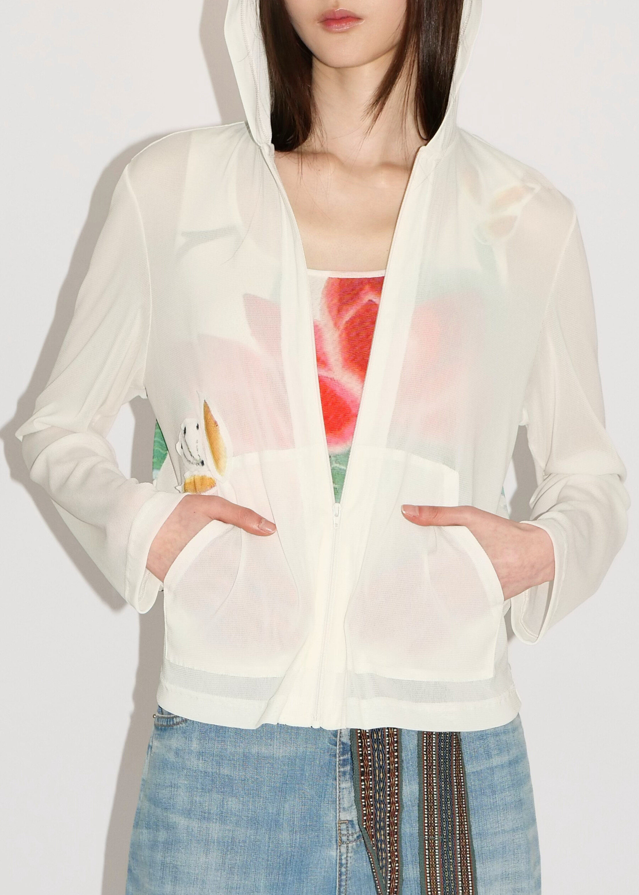 Woman wearing a white hoodie with a colorful design underneath on a plain background