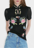 Woman wearing a black embroidered top with floral designs on a white background