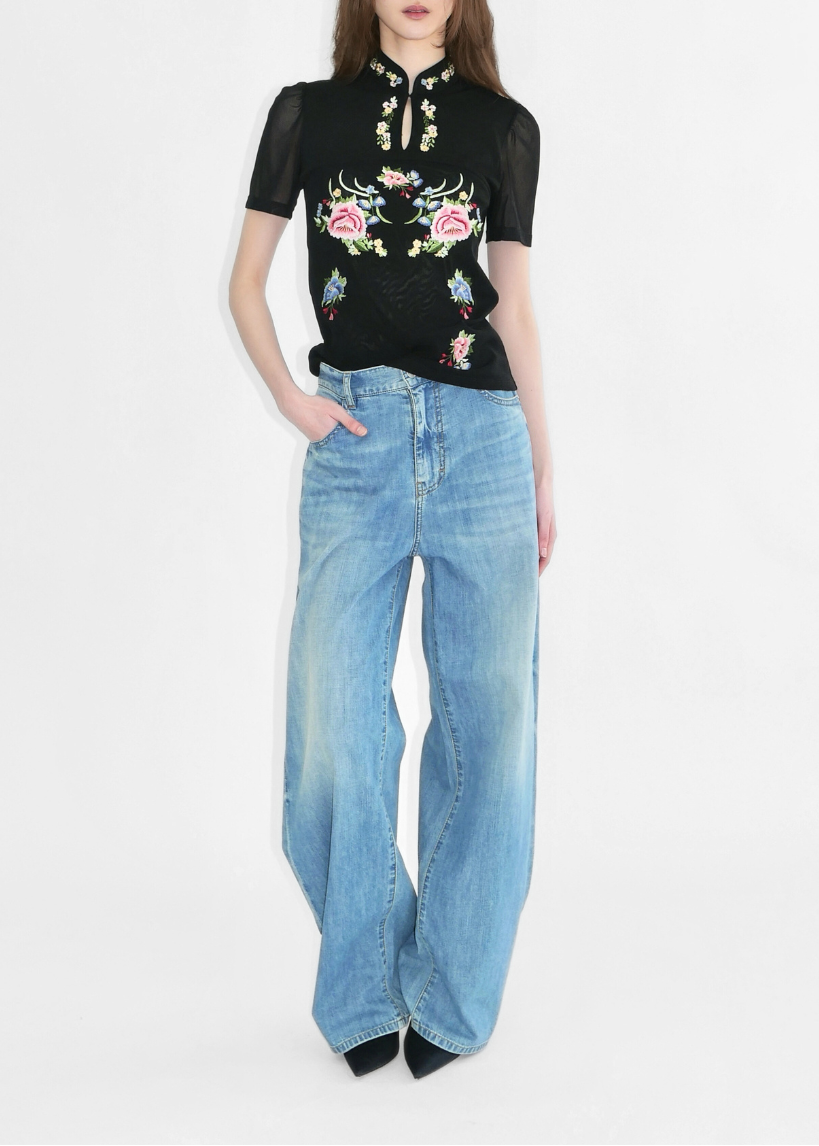 Woman wearing a black embroidered top and blue jeans on a white background