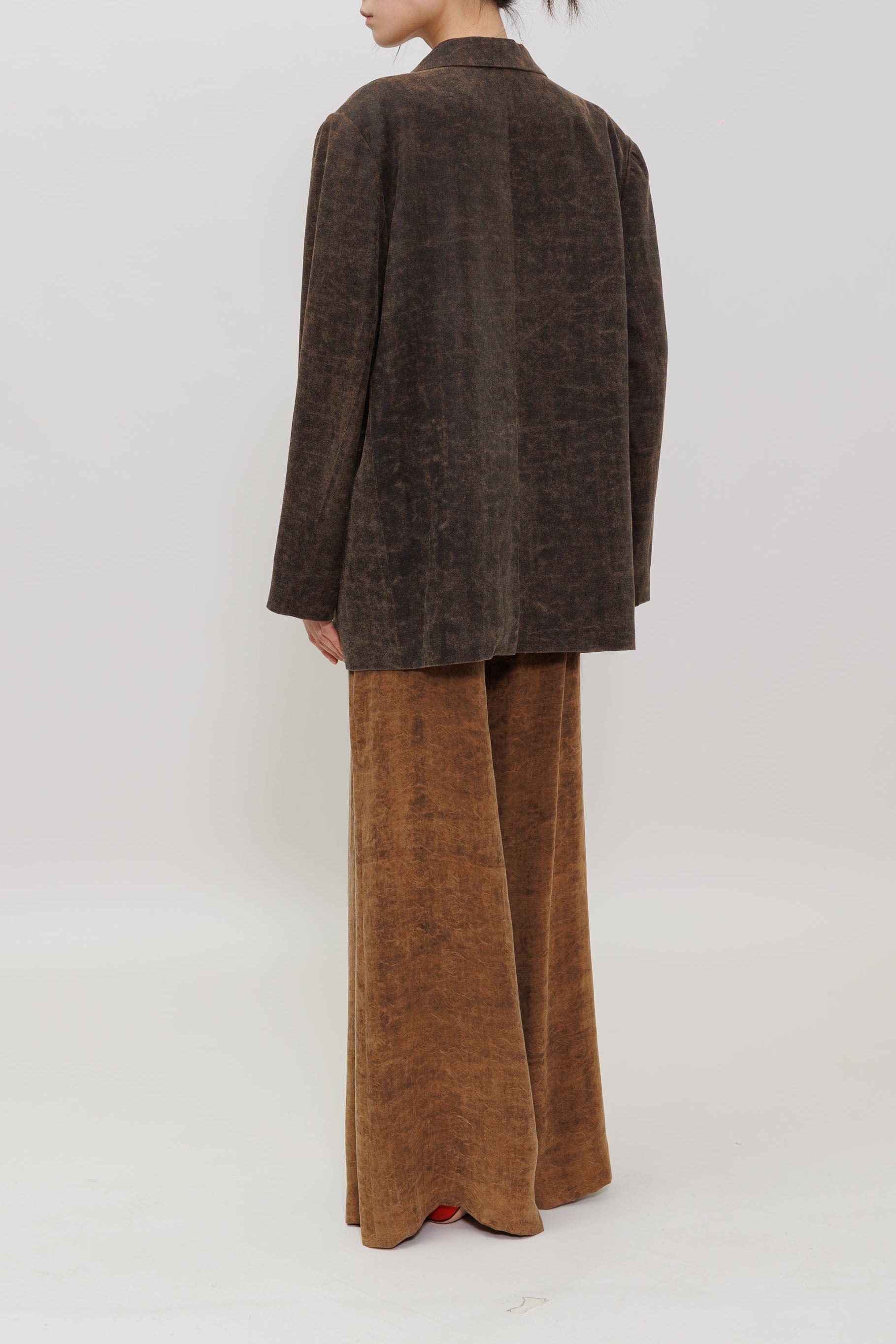 A model is shown from the back wearing a dark brown textured blazer and matching wide-leg trousers against a plain light gray studio background.