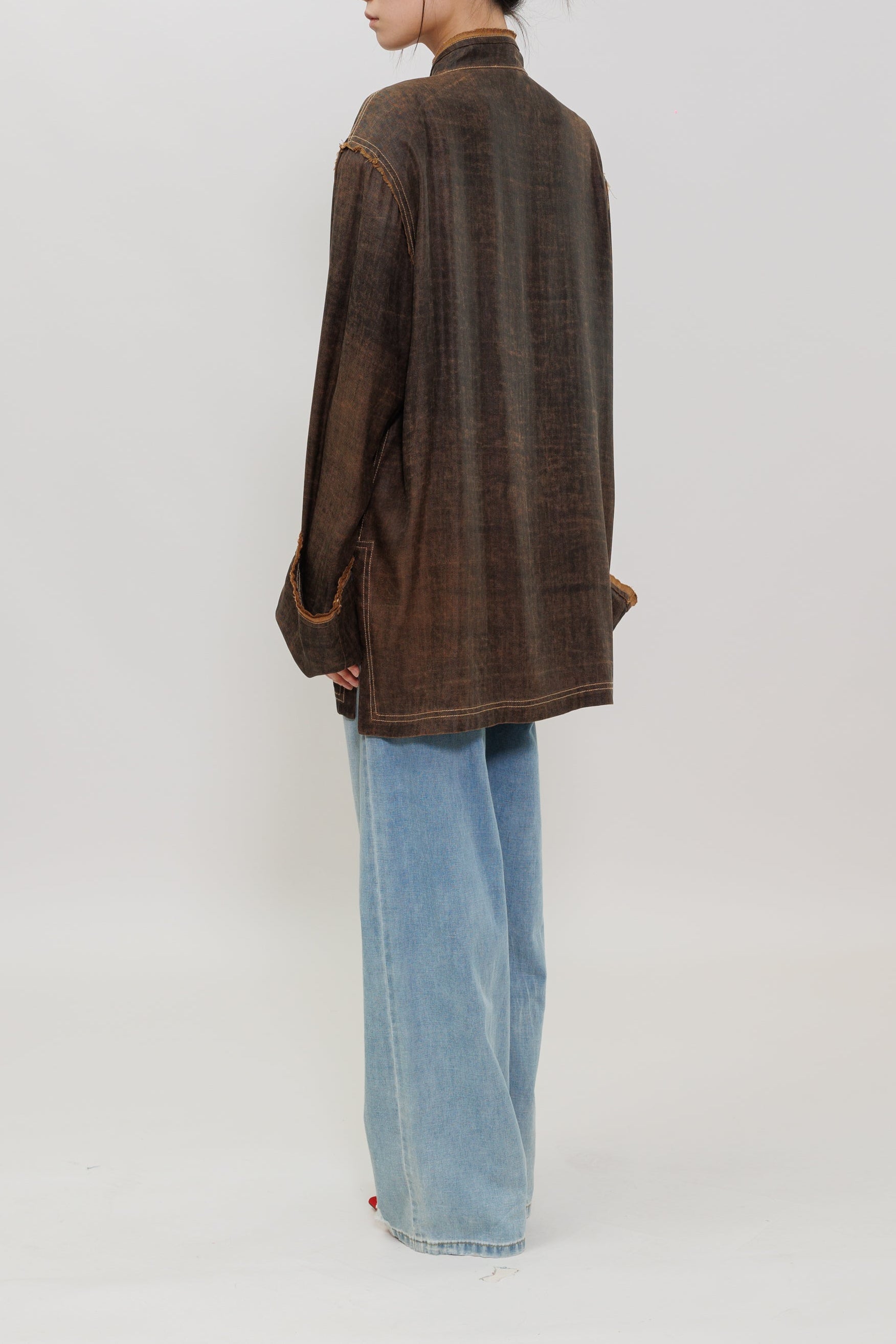 A model stands in profile wearing a brown textured, long-sleeve button-up shirt and wide-leg light blue jeans against a plain white studio background.