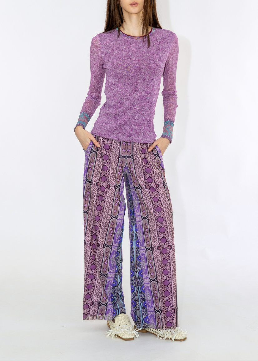 Woman wearing a purple long-sleeve top and patterned pants on a white background
