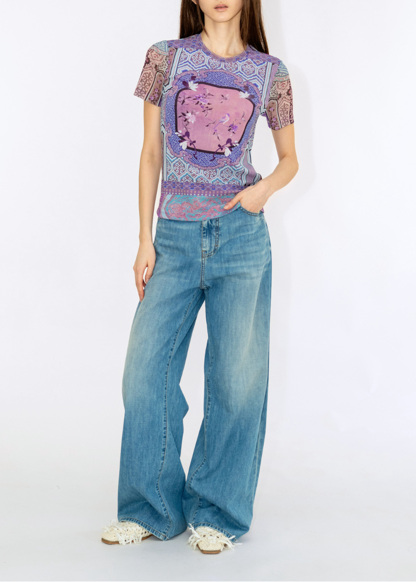 Woman wearing a patterned top and blue jeans on a white background