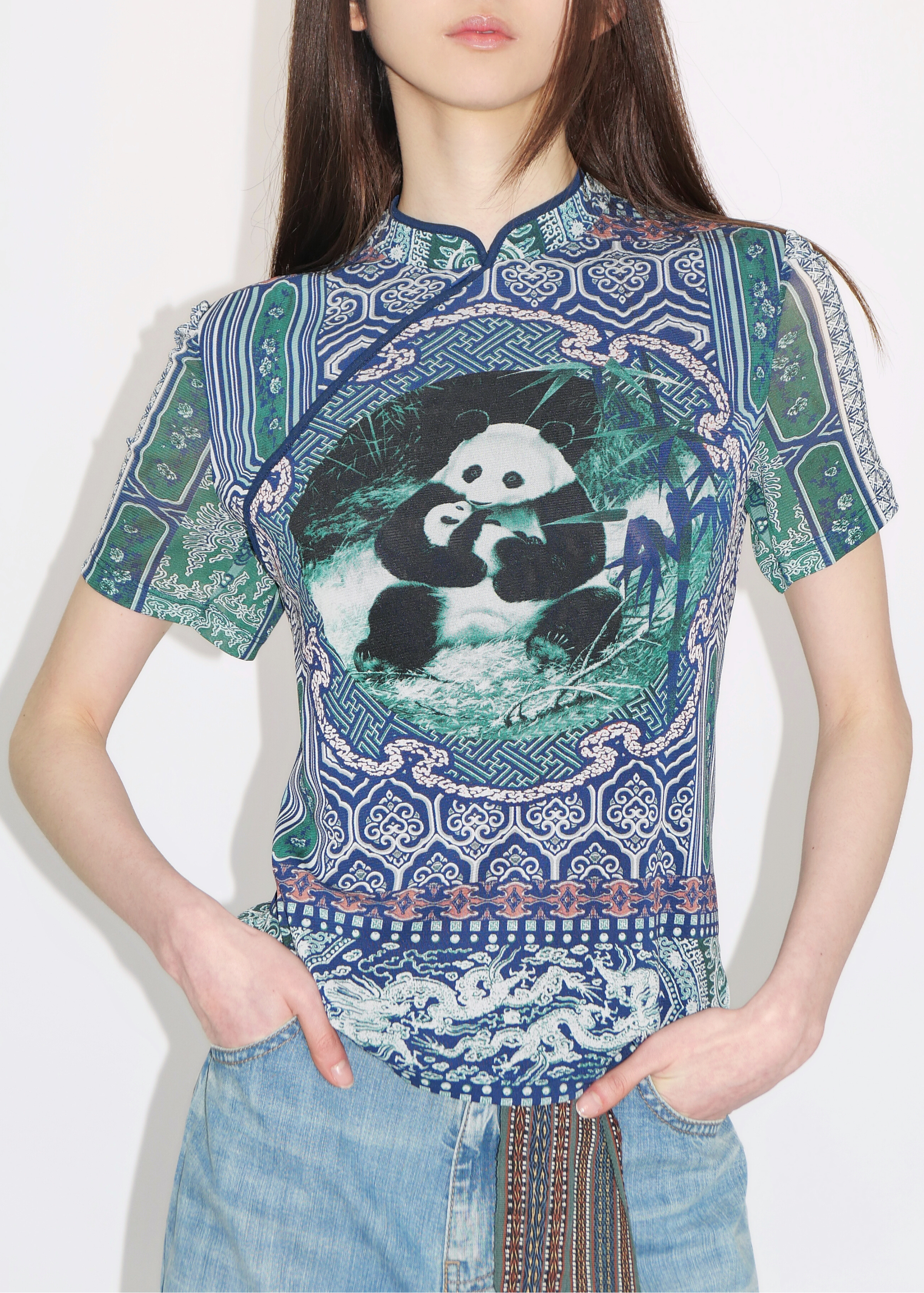 A woman wearing a multicolored traditional Chinese cheongsam top with a panda pattern, paired with blue jeans.