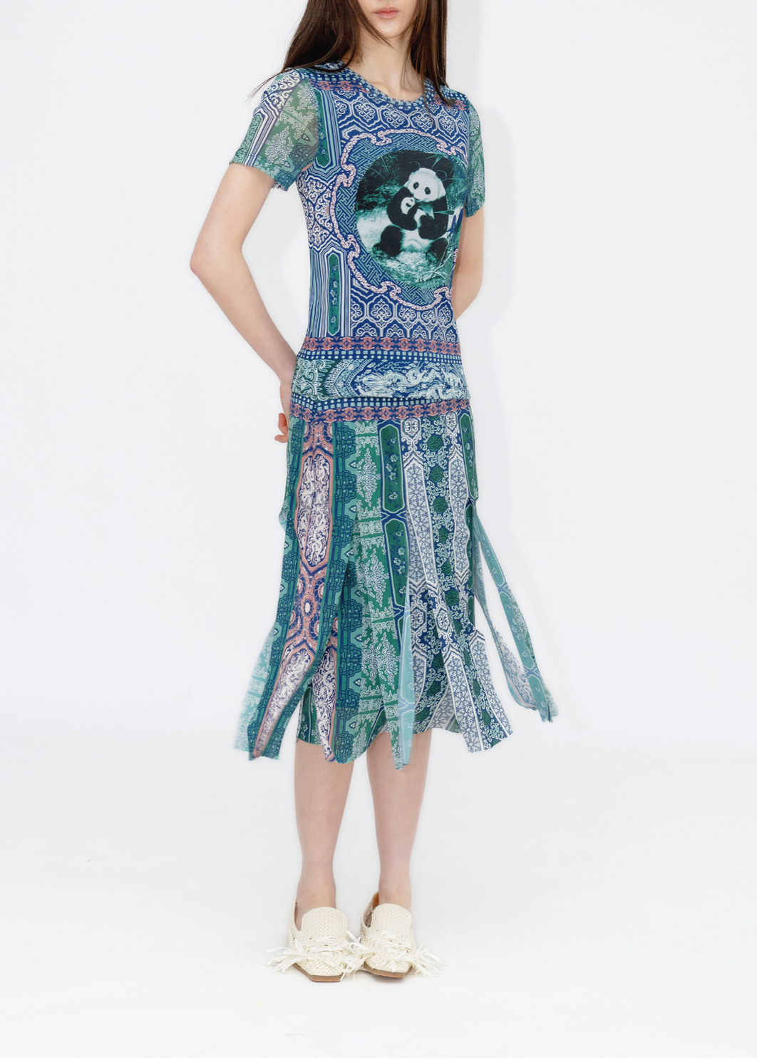 A woman standing against a white background, wearing a geometric patterned skirt with a character graphic top.