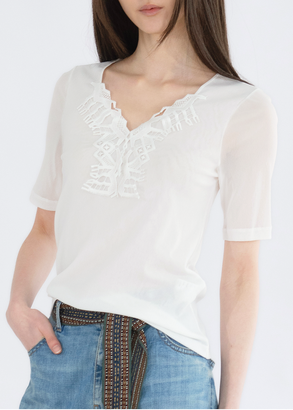 A woman wearing a white solid top with deer lace detailing, paired with blue jeans.