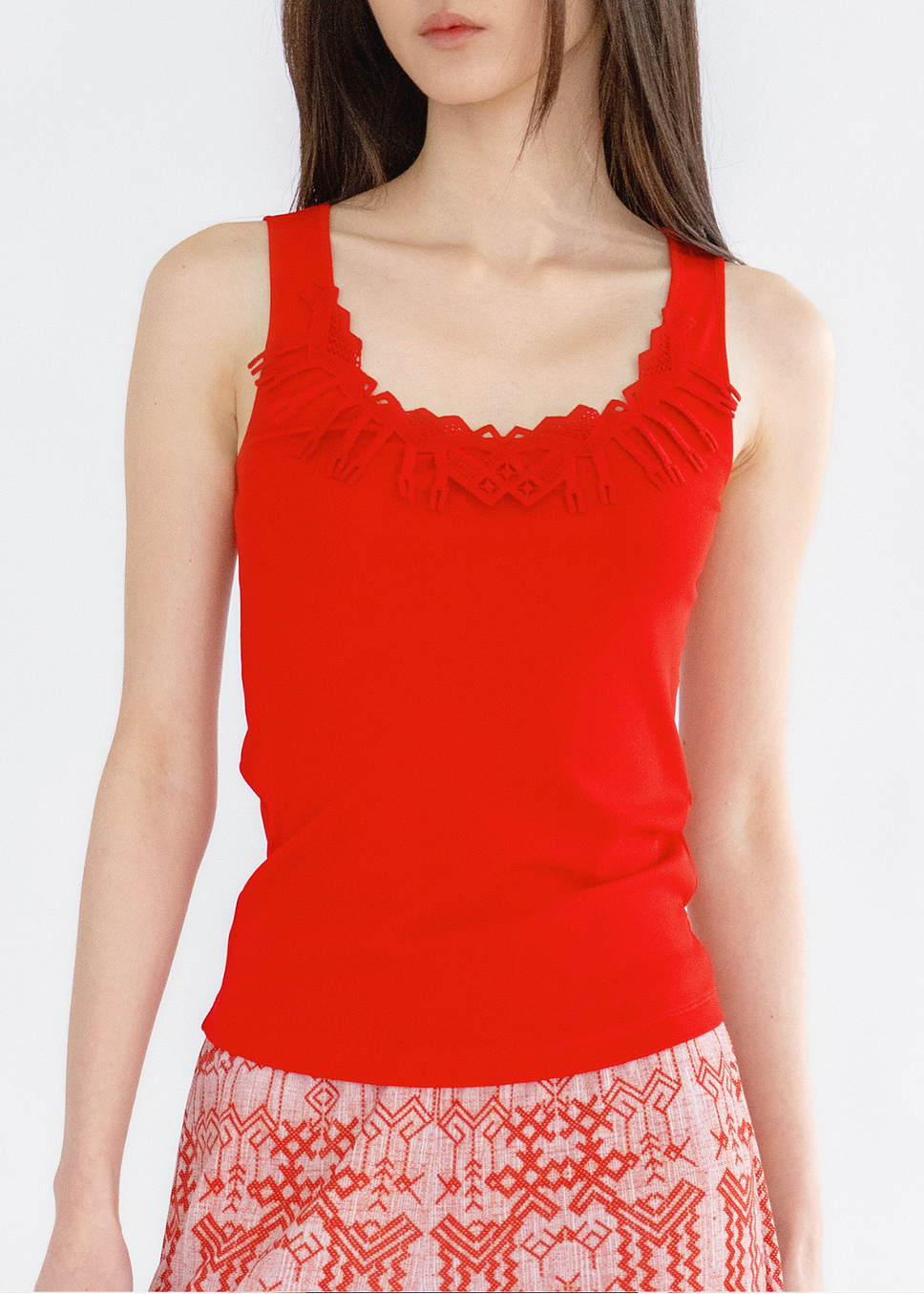 A woman wearing a red solid tank top with deer lace detailing at the neckline.