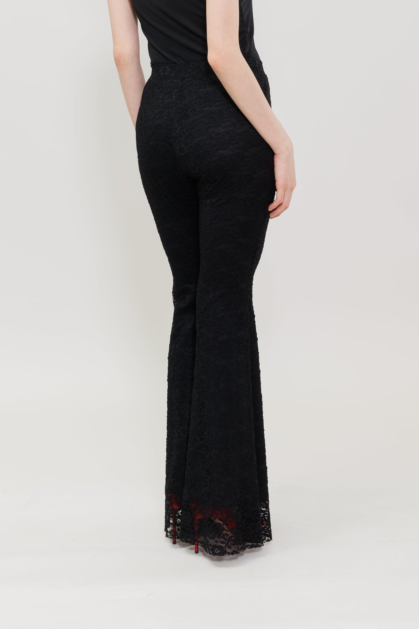A model is shown from the back wearing a black spaghetti-strap sleeveless jumpsuit with a flared silhouette, set against a plain light gray studio background.