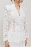 A woman wearing a white lace long-sleeve wrap blazer with a matching tie belt, shown from the chest down against a plain light gray studio background.