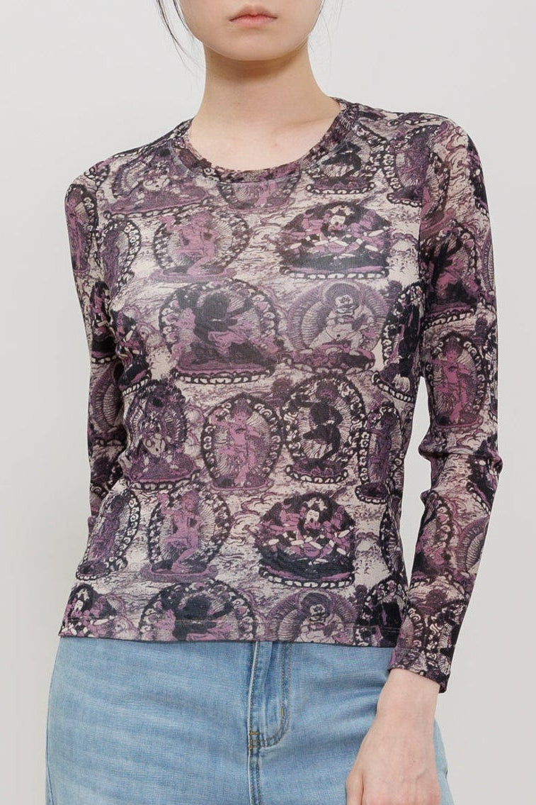 A model wearing a long-sleeve crewneck top with a purple and black paisley pattern, paired with light-wash wide-leg jeans, photographed against a neutral light gray studio background.