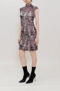 A model stands against a plain light gray studio background wearing a sleeveless high-neck mini dress with a purple and gray abstract pattern, paired with black ankle socks and black pointed heels.