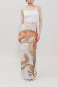 A model stands against a plain light gray studio background wearing a white spaghetti-strap maxi dress with a large printed dragon design in beige, brown, and red tones on the lower half.